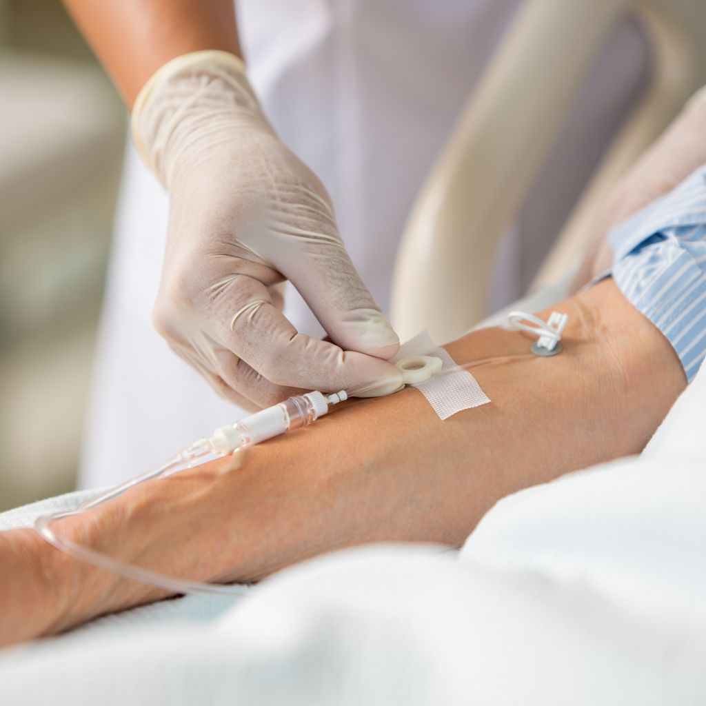 Медсестра в стерильных перчатках фиксирует катетер на предплечье пациента